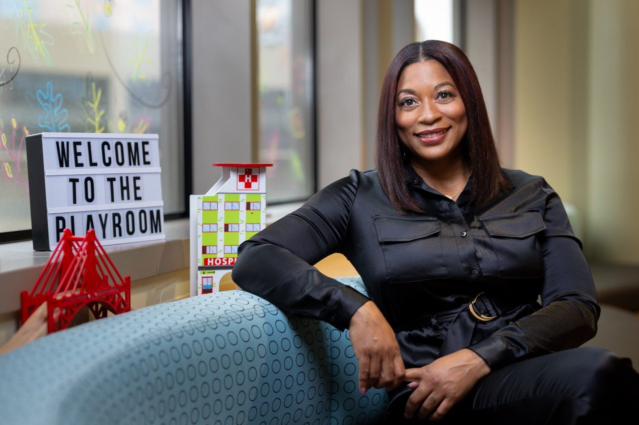 Tomika Gamble is pictured sitting on a sofa next to a sign that says Welcome to the Playroom..