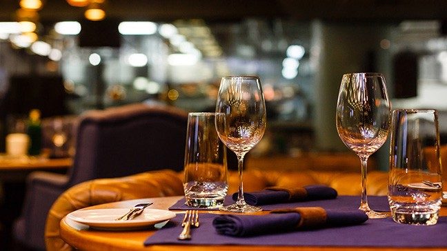 Two empty wine glasses and water glasses sit atop a table next to purple napkins, a white plate and silverware